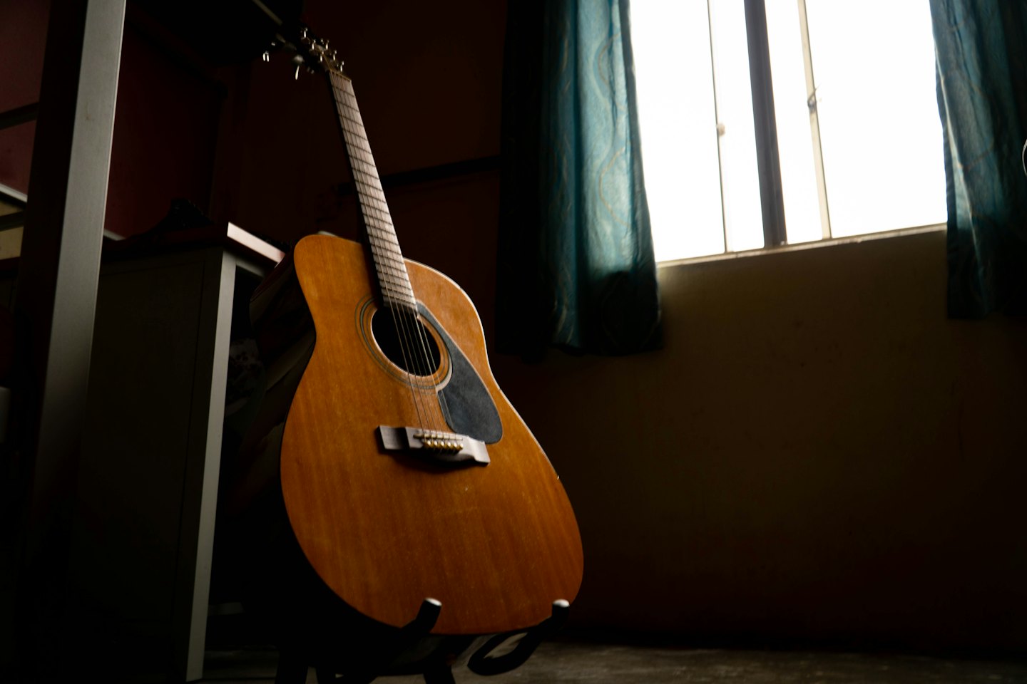 Acoustic wooden guitar standing upright on a metal floor stand.